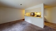 This single-floor residential unit offers a practical and comfortable layout across several well-defined living spaces. The living area is generously sized, featuring plush wall-to-wall carpeting and a large sliding glass door fitted with vertical blinds that fills the room with natural light. A built-in pass-through counter connects the living area to the kitchen, creating an open, communicative flow between the two spaces.

The galley-style kitchen is efficiently designed with cream-colored cabinetry, laminate countertops, and rich hardwood-style flooring. It is equipped with black appliances including a refrigerator, electric range with overhead microwave, and dishwasher, along with a stainless steel double sink. The kitchen leads directly to the unit's entry door, adding convenient accessibility.

Multiple bedrooms are carpeted and finished with neutral tones, each featuring windows with horizontal blinds that allow for ample natural light and outdoor views of surrounding greenery. The rooms offer versatile layouts suited for a variety of furniture arrangements.

Two full bathrooms mirror each other in design, each featuring a single-sink vanity with cream cabinetry, a tub-shower combination with white tile surround, hardwood-style flooring, and overhead lighting. The overall aesthetic throughout the unit is clean, neutral, and move-in ready.