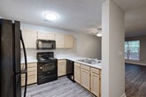 Located at 2505 Fairfax Rd in Greensboro, NC, this one-bedroom, one-bathroom unit offers a well-organized single-floor layout designed for comfortable everyday living. The open-concept kitchen and living area form the heart of the space, connected by a peninsula counter that provides both additional workspace and a casual dining option. The kitchen is outfitted with light wood cabinetry, white countertops, and a full suite of black Whirlpool appliances, including a refrigerator, electric range, over-the-range microwave, and dishwasher. Durable wood-style plank flooring runs throughout the kitchen and living areas, while a textured ceiling adds a classic finish overhead. The living room benefits from a large window overlooking a wooded outdoor area, filling the space with natural light, and a ceiling fan adds year-round comfort. The bedroom is generously proportioned, featuring soft wall-to-wall carpeting, a ceiling fan with light fixture, a window with greenery views, and access to multiple closets — notably five closets total throughout the unit, offering exceptional storage. A dedicated utility room adds further practicality. Neutral gray walls throughout lend the space a clean, move-in-ready aesthetic.
