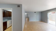 Located at 611 E Ailsie Ave in Kingsville, Texas, this single-floor residence offers a clean, functional layout with a consistent design palette throughout. The interior is finished with light tan ceramic tile flooring across all rooms, complemented by cool gray-blue painted walls and crisp white baseboards that create a cohesive and neutral aesthetic.

The living area is generously proportioned, benefiting from a sliding glass door fitted with vertical blinds that allows abundant natural light to fill the space. An adjacent area provides additional room suitable for dining or flexible use, with a window that further contributes to the bright interior.

The galley-style kitchen is efficiently designed, featuring dark wood cabinetry on both sides, laminate countertops, a double-basin sink, and white appliances including a refrigerator, range, and dishwasher. The layout maximizes counter and storage space within a compact footprint.

The bedrooms are well-sized and finished in the same neutral tones, with at least one room featuring a wide closet equipped with a full-width hanging rod and built-in shelving above, providing practical storage. The bathroom includes a tub and shower combination with full tile surround in a warm beige tone, chrome fixtures, and tile flooring that coordinates with the rest of the home. Central HVAC vents are present throughout, ensuring climate comfort across the entire floor plan.