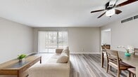 This single-floor, 2-bedroom space offers a clean, neutral aesthetic with light-toned walls and durable hardwood-style flooring carried consistently throughout. The open-concept living and dining area serves as the heart of the home, bathed in natural light streaming through a large sliding glass door fitted with vertical blinds that open to an outdoor view. A ceiling fan overhead adds both function and a finishing touch to the living space.

The kitchen is efficiently designed with white shaker-style cabinetry, granite-look countertops, and a full suite of stainless steel appliances including a refrigerator, range, and dishwasher. A window above the sink brings in additional natural light, making the space feel bright and practical.

The generously sized primary bedroom comfortably accommodates large furniture and features a ceiling fan, a window with blinds, and direct access to a dedicated walk-in closet outfitted with dual hanging rods. The second bedroom is equally well-proportioned, with a ceiling fan, built-in shelving nook, and the same warm flooring found throughout the space.

The dining area adjoins the living room in an open layout, providing a seamless flow ideal for everyday living and entertaining. Overall, the space presents a cohesive, modern, and move-in-ready environment with functional design at its core.