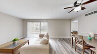 This single-floor, 2-bedroom space offers a clean, neutral aesthetic with light-toned walls and durable hardwood-style flooring carried consistently throughout. The open-concept living and dining area serves as the heart of the home, bathed in natural light streaming through a large sliding glass door fitted with vertical blinds that open to an outdoor view. A ceiling fan overhead adds both function and a finishing touch to the living space.

The kitchen is efficiently designed with white shaker-style cabinetry, granite-look countertops, and a full suite of stainless steel appliances including a refrigerator, range, and dishwasher. A window above the sink brings in additional natural light, making the space feel bright and practical.

The generously sized primary bedroom comfortably accommodates large furniture and features a ceiling fan, a window with blinds, and direct access to a dedicated walk-in closet outfitted with dual hanging rods. The second bedroom is equally well-proportioned, with a ceiling fan, built-in shelving nook, and the same warm flooring found throughout the space.

The dining area adjoins the living room in an open layout, providing a seamless flow ideal for everyday living and entertaining. Overall, the space presents a cohesive, modern, and move-in-ready environment with functional design at its core.