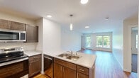 Located at 375 Autumn Pond Way in Essex Junction, Vermont, this two-bedroom, one-bathroom residence offers a thoughtfully laid-out single-floor plan with modern finishes throughout. The open-concept kitchen and living room serve as the heart of the home, featuring warm hardwood-style flooring, recessed lighting, and pendant fixtures. The kitchen is equipped with stainless steel appliances — including a refrigerator, range, and microwave — complemented by rich dark cabinetry, light countertops, and a double-basin sink set into a peninsula with additional prep space. The living room is bright and airy, with large windows and a glass door that opens to a balcony, filling the space with natural light and views of surrounding greenery. Both bedrooms continue the warm flooring aesthetic, with neutral walls and windows that allow ample natural light. The primary bedroom offers a comfortable footprint with a closet for storage. The full bathroom features a tub-shower combination and clean white finishes, with a stacked in-unit washer and dryer conveniently included. The overall design is clean and contemporary, providing a functional and comfortable living environment in a peaceful Vermont community.