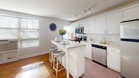 This single-floor unit offers a well-designed layout that maximizes both functionality and comfort. The open-concept living and kitchen area serves as the heart of the space, where warm hardwood floors and white-painted walls create a clean, inviting atmosphere. Natural light streams in through multiple windows fitted with blinds throughout the unit.

The kitchen is thoughtfully equipped with white cabinetry extending to the ceiling, stainless steel appliances including a refrigerator, range, microwave, and dishwasher, and a light-toned countertop peninsula with seating for two. Track lighting overhead provides additional illumination for the workspace. The peninsula connects seamlessly to the living area, which offers an open, relaxed setting with ample room for seating.

The bedroom is a calm and comfortable retreat, featuring hardwood flooring, generous natural light from large windows, and neutral walls that lend a serene quality to the room. The bathroom is clean and efficiently laid out, finished with white tile, a walk-in shower, a vanity with storage cabinetry, and recessed lighting. A closet adjacent to the bathroom provides convenient storage. Throughout the unit, the consistent use of white tones and natural wood flooring creates a cohesive, bright, and livable environment.