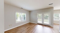 This well-appointed two-bedroom, two-bathroom residence at Residences On Carr Hill in Columbus, Indiana, offers a thoughtfully designed single-floor layout with a clean, contemporary aesthetic throughout. Neutral gray walls, white trim, and wood-look plank flooring in the main living areas create a cohesive and modern feel.

The living room is generously proportioned, featuring multiple windows alongside French doors that flood the space with natural light and provide views of surrounding greenery. The kitchen is efficiently laid out with white shaker-style cabinetry, granite-look countertops, and stainless steel appliances, including a range, microwave, and refrigerator.

The primary bedroom features vaulted ceilings, a ceiling fan, and large windows, complemented by plush carpeting. It is served by a dedicated bathroom with a granite-topped vanity, framed mirror, and open shelving beneath. A spacious walk-in closet with wire shelving provides ample storage. The second bedroom also features carpet and a natural light-filled window. A connecting hallway with light wood flooring links the rooms efficiently, contributing to the unit's practical and comfortable flow.