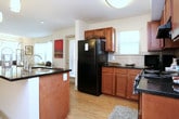 This single-story residence offers a thoughtfully designed layout that balances comfort and functionality across its living spaces. The kitchen is a standout feature, showcasing rich medium-toned wood cabinetry, dark granite countertops, a tile backsplash, and black appliances including a refrigerator, electric range, and dishwasher. An island with a built-in sink adds additional prep space, while wood-look flooring and windows providing outdoor views contribute to a bright, welcoming atmosphere.

The living area is well-lit by multiple windows dressed with sheer curtains and blinds, allowing ample natural light to fill the room. A secondary sitting nook near the entry offers additional flexible space with views to the outdoors.

The bedroom is comfortably sized and features carpet flooring, a ceiling fan, and a window that invites natural light. A dedicated walk-in closet provides generous storage. The bathroom includes a tub-shower combination with tile flooring and warm neutral finishes throughout.

A notable convenience is the in-unit laundry area, which houses a stacked full-size washer and dryer. Neutral wall tones and consistent flooring materials tie the space together, creating a cohesive and livable environment throughout.