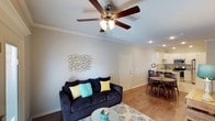 This single-story, two-bedroom, one-bathroom space offers a thoughtfully designed layout that maximizes functionality and comfort. The open-concept living and dining area forms the heart of the home, where hardwood-style flooring runs continuously underfoot, adding warmth and a cohesive aesthetic throughout. Crown molding frames the ceilings, lending a polished, refined character to the space.

The living area is generously proportioned, featuring a ceiling fan with a light fixture that provides both airflow and ambient lighting. Recessed lighting complements the overall brightness of the room. Neutral wall tones create a versatile backdrop, allowing for a range of décor styles.

The dining area flows naturally from the living space, accommodating a dining table with ease and providing a seamless transition toward the kitchen, which is visible in the background and features white cabinetry and countertop space suited for everyday cooking needs.

The layout includes two bedrooms, offering flexible use of space whether for sleeping, working, or guests. The single bathroom serves the unit efficiently. Overall, the space presents a clean, move-in-ready environment with classic architectural details and a warm, inviting ambiance.