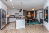 Located in Atlanta's Old Fourth Ward neighborhood, this single-floor unit at 600 Arnold St NE showcases a cohesive modern design with clean lines and a carefully curated color palette. The open-concept kitchen is a standout feature, outfitted with flat-front white cabinetry extending to the ceiling, dark granite countertops, a geometric hexagonal tile backsplash, and a full suite of stainless steel appliances including a gas range, microwave, and French door refrigerator. A central island with bar seating and stylish pendant lighting serves as a natural gathering point and transitions seamlessly into the living area. The living room features a dark accent wall, large windows with natural light, and an inviting sectional sofa paired with a teal vintage-style area rug. Light hardwood flooring runs throughout the main living spaces, adding warmth and continuity. The primary bedroom offers plush carpeting, a dramatic teal upholstered headboard, a ceiling fan, and ample natural light. A second bedroom provides a bright, versatile space with open shelving. The bathroom features an elongated double vanity with dark countertops, white cabinetry, black hardware, and pendant lighting, maintaining the unit's consistent contemporary aesthetic.