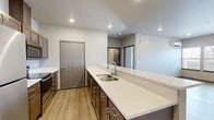 Located at 3027 E Upriver Dr in Spokane, WA, this well-appointed one-bedroom, one-bathroom unit offers a thoughtfully designed single-floor layout. The open-concept kitchen and living area serves as the heart of the home, anchored by a generous island with a quartz countertop, a double stainless steel sink, and dark wood cabinetry. Stainless steel appliances—including a refrigerator, electric range, and microwave—complete the kitchen, which flows seamlessly into the living area. Light wood-look flooring runs throughout the entire unit, lending a cohesive, modern aesthetic. The spacious living room is bright and airy, with windows and a glass-panel door that invite natural light and provide outdoor views. A wall-mounted mini-split unit ensures efficient heating and cooling year-round. The primary bedroom is a comfortable, well-sized retreat with recessed lighting, a mini-split system, and continued wood-look flooring. The bathroom features a dark wood vanity with a white countertop, a lighted mirror, and a walk-in shower. Conveniently, an in-unit washer and dryer are tucked just off the bathroom, adding practical functionality to this clean, contemporary home.