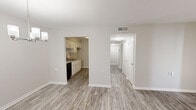 Located at 1449 Richland Rd in Auburn, Alabama, this 2-bedroom, 1-bathroom single-story home offers a well-organized layout with a clean, modern aesthetic. The interior is finished with light gray wood-look flooring throughout the main living areas, crisp white walls, and white baseboards that give the space a bright, cohesive feel. The open living room connects seamlessly to the dining area, which is accented by a contemporary chandelier with frosted glass shades, adding a touch of elegance. The galley-style kitchen is efficiently designed with white shaker cabinetry, granite-style countertops, a stainless steel sink, black appliances including an electric range and dishwasher, and a subway tile backsplash — all flowing directly into the dining space. A hallway leads to both bedrooms and the bathroom. The primary bedroom is a comfortable size and features its own closet with bi-fold doors and soft carpet flooring. The second bedroom is finished with the same wood-look flooring as the main living areas. The bathroom includes a tiled tub-shower combination. Additional storage is available through a dedicated closet fitted with multiple built-in shelves. The overall ambiance is clean, functional, and move-in ready.