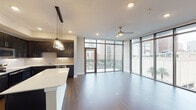 This single-floor, two-bedroom, two-bathroom residence offers a well-designed layout with a blend of modern finishes and urban character. The open-concept living and dining area is anchored by rich dark hardwood flooring and flows seamlessly toward a wall of floor-to-ceiling windows and a glass-paneled balcony door, framing sweeping city skyline views and filling the space with abundant natural light. A ceiling fan complements the airy feel of the main living area.

The kitchen is a standout feature, showcasing dark espresso cabinetry, a classic tile backsplash, stainless steel appliances, and a generous white quartz island illuminated by a cluster of contemporary glass pendant lights. A tray ceiling detail adds architectural interest overhead.

Both bedrooms are carpeted and well-proportioned, each receiving natural light through large windows with urban views. The primary bathroom is finished with marble-look tile flooring, a soaking tub with matching surround, a dual-sink vanity with dark cabinetry, and tall storage towers. The second bathroom mirrors this aesthetic with marble-look tile and a tub-shower combination. Neutral wall tones throughout the residence create a cohesive, modern atmosphere.