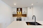 Located at 1330 S Fair St in Arlington, VA, this thoughtfully designed one-bedroom, one-bathroom residence offers a clean, contemporary aesthetic throughout. Light wood-look flooring flows seamlessly across the open-concept living area, connecting the living room, dining space, and kitchen into a cohesive and functional layout. The kitchen is a standout feature, showcasing flat-front white cabinetry with matte black hardware, a warm wood-toned backsplash, stainless steel range with a sleek hood vent, and a large center island with a white quartz countertop, undermount sink, and dark cabinetry base. Natural light pours in through floor-to-ceiling sliding glass doors that open to a private balcony, offering open views of the Arlington skyline. The bedroom is a bright, comfortable retreat with dual windows framing urban views and includes a built-in Murphy bed cabinet. Two closets provide generous storage, including a walk-in closet outfitted with adjustable shelving and hanging rods. The bathroom features tile flooring, a sleek dark-toned vanity with integrated sink, and direct access to the walk-in closet. In-unit laundry adds everyday convenience. Clean white walls and recessed lighting throughout contribute to a bright, modern ambiance.