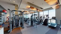 Located in Chicago's vibrant West Loop neighborhood, this fitness center at 933 W Washington Blvd offers a thoughtfully designed, single-floor facility equipped for a full range of workout routines. The space is defined by expansive floor-to-ceiling windows that line the perimeter, flooding the interior with natural light and providing striking elevated views of the surrounding Chicago skyline and cityscape.

The cardio zone features a row of modern ellipticals, stair climbers, and additional aerobic machines positioned directly in front of the windows, allowing users to exercise while taking in panoramic city views. Distinctive sculptural wood-and-fabric pendant light fixtures hang from the ceiling, adding warmth and an architectural focal point to the space.

The strength training area is comprehensively outfitted with multi-function cable machines, a smith machine, and a full rack of TAG dumbbells ranging across a wide weight spectrum. Full-length mirrors line interior walls, enhancing the sense of openness and providing visual feedback during workouts. A dedicated free weights section includes adjustable benches and specialty strength equipment.

A separate, glass-partitioned studio space is accessible via black-framed doors, offering additional room for group fitness, cycling, or functional training. The overall design balances a polished, upscale aesthetic with practical, performance-oriented functionality.