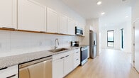 This single-floor unit presents a clean, contemporary design highlighted by light hardwood flooring and bright white walls that create a cohesive, airy aesthetic throughout. The galley-style kitchen is well-equipped with stainless steel appliances, including a French door refrigerator, electric range, built-in microwave, and dishwasher. White shaker-style cabinetry extends to the upper walls, offering generous storage, while speckled granite countertops and a horizontal subway tile backsplash add refined detail. A single-basin sink with a brushed nickel faucet completes the functional workspace.

The open living area is a standout feature, bathed in natural light from floor-to-ceiling black-framed windows and a glass door that opens directly onto a balcony with open city views. Recessed lighting supplements natural light throughout. A separate bedroom provides a quiet, well-sized retreat with recessed lighting and direct access to a laundry area. The bathroom mirrors the kitchen's design language, featuring matching granite countertops, white cabinetry, a large vanity mirror, and a full tub-shower combination, all finished with the same light hardwood flooring found throughout the unit.