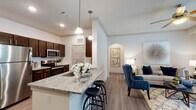 Located on Whaley Drive in Forney, Texas, this single-floor residence offers a thoughtfully designed open-concept layout that seamlessly connects the kitchen, dining, and living areas. The kitchen is a standout feature, boasting rich dark-brown cabinetry, granite countertops, stainless steel appliances — including a refrigerator, microwave, and range — and a center island with bar seating and a pendant-lit overhang, ideal for casual dining or entertaining. The adjoining dining nook provides an intimate setting with crown molding details that carry throughout the common areas. The living room is bright and welcoming, enhanced by natural light from large windows with blinds, crown molding, and direct access to an outdoor balcony through a glass-panel door. A dedicated home office features carpet flooring, dual windows, and a ceiling fan, offering a quiet and functional workspace. The bathroom is finished with dark wood vanity cabinetry, granite countertops, a large mirror with overhead lighting, and light wood-tone flooring. Consistent light wood-tone flooring flows through the main living spaces, tying the interior together with a clean, modern aesthetic. A double-door closet provides generous storage within the unit.