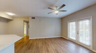This single-floor residence offers a well-designed, functional layout that balances open living spaces with comfortable private areas. The main living room is bright and welcoming, featuring warm hardwood-style flooring, neutral-toned walls, a ceiling fan with integrated lighting, and a window fitted with blinds that brings in natural light while offering privacy. French doors open to the exterior, enhancing the connection between indoor and outdoor spaces.

The kitchen is a standout feature, designed with an open-concept approach that flows seamlessly into the living area. It is equipped with stainless steel appliances, including a refrigerator, microwave, and electric range, complemented by crisp white cabinetry, a light-colored countertop peninsula, and hardwood-style flooring that continues from the living space.

The bedrooms provide a more subdued, restful atmosphere, finished with plush wall-to-wall carpet and neutral walls. One bedroom benefits from a window with views of lush greenery, adding a refreshing natural element to the room.

The bathroom is finished with hardwood-style flooring, white cabinetry, and a full tub-shower combination featuring a classic tiled surround with a decorative checkered accent border, completing the space with a clean, practical design.