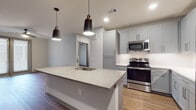 This single-floor residence showcases a contemporary design with a cohesive neutral palette and high-quality finishes throughout. The open-concept kitchen serves as the centerpiece, featuring a generously sized island with a white quartz countertop, an undermount sink, and dramatic matte black pendant lighting. Gray shaker-style cabinetry extends to the ceiling, providing ample storage, while stainless steel appliances—including a range, built-in microwave, and French door refrigerator—complete the space. Wood-look flooring flows seamlessly throughout the living and bedroom areas, adding warmth and visual continuity.

The living area is bright and airy, benefiting from large windows and a sliding glass door that invites natural light and outdoor access. A ceiling fan enhances comfort in this space. The bedrooms are well-proportioned, each featuring dual windows with blinds and the same wood-look flooring.

The bathrooms are thoughtfully appointed with large-format white tile flooring, warm wood-toned vanities, and white countertops. One bathroom includes a soaking tub with subway tile surround, while another features a glass-enclosed walk-in shower. A walk-in closet with built-in shelving is accessible directly from one of the bathrooms, adding practical storage solutions to the overall design.