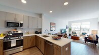 Located at 1401 Kings Hwy in Fairfield, Connecticut, this thoughtfully designed single-floor residence combines modern aesthetics with functional living. The open-concept layout seamlessly connects the kitchen, dining, and living areas, creating a fluid and inviting atmosphere throughout.

The kitchen is a standout feature, equipped with stainless steel appliances including a gas range, microwave, and refrigerator. Two-tone cabinetry pairs warm wood lower cabinets with sleek grey upper units, complemented by light quartz countertops and a peninsula island ideal for casual dining or food preparation. Light hardwood-style flooring runs throughout the main living areas, enhancing the bright, airy feel.

The living room is filled with natural light streaming through large picture windows that frame outdoor views, creating a welcoming retreat. The space flows effortlessly into the dining area, which comfortably accommodates a full dining set.

The bedrooms are well-proportioned and serene, featuring plush carpeting, generous windows with outdoor views, and ample closet space including walk-in storage. The bathroom is clean and contemporary, featuring a soaking tub and shower combo, a floating vanity with an undermount sink, and wood-look flooring that ties the design together cohesively.