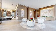 Astra Tower's ground-floor lobby is a masterfully designed entrance experience that immediately conveys a sense of luxury and refinement. Accessed through sleek, stainless steel-framed glass doors at address number 89, the space opens into a generously proportioned interior defined by soaring ceilings and floor-to-ceiling glass curtain walls that flood the area with natural light and frame views of the surrounding urban cityscape.

At the heart of the lobby sits a striking marble reception desk, positioned beneath the boldly displayed "Astra Tower" signage, which is dramatically accented by a sculptural wall installation of cascading floral elements. Warm, wood-paneled walls provide a refined backdrop throughout, complemented by large-format stone tile flooring in soft, neutral tones.

The main seating lounge features a curated arrangement of plush, cream-colored swivel chairs centered around a dark, fluted cylindrical coffee table atop a circular area rug, creating an inviting and cohesive gathering area. Framed abstract artwork with warm pink and terracotta tones lines the walls, adding artistic depth to the space.

A dedicated mail room offers practical functionality, lined with dark bronze mailboxes on three walls beneath a double-height ceiling adorned with ink-wash landscape murals, all centered around a long white sorting table. The overall ambiance is polished, contemporary, and welcoming.