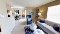 This single-story residence offers a well-organized layout with distinct living, dining, kitchen, and sleeping areas connected by a cohesive neutral color palette of warm beiges and soft whites. The living room is carpeted and features large windows that allow natural light to fill the space, built-in corner shelving, and a textured ceiling. The open sightline connects the living area to the dining space, which accommodates a round table and benefits from a sliding glass door fitted with vertical blinds, providing access to an outdoor area.

The galley-style kitchen runs along two parallel walls lined with warm wood cabinetry and light countertops, offering generous storage and counter space alongside tile flooring and built-in appliances. Two bedrooms are each carpeted and include ceiling fans with light fixtures and windows for natural light. The primary bedroom is notably spacious, while the secondary bedroom is comfortably sized.

Two bathrooms mirror each other in design, each featuring a wide vanity with a single sink, wood cabinetry, a large mirror, overhead lighting, and tile flooring. One bathroom includes a walk-in shower, while the other offers additional overhead cabinet storage, providing practical functionality throughout.