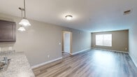 Located at 1034 Finnwood Dr in Whitsett, NC, this single-floor, one-bedroom, one-bathroom home offers a thoughtfully designed layout that maximizes every square foot of living space. The open-concept living, dining, and kitchen area forms the heart of the home, featuring durable wood-look plank flooring throughout and neutral warm-toned walls that create a clean, welcoming atmosphere. A window allows natural light to brighten the living area, which also benefits from a ceiling-mounted light fixture for added illumination. The kitchen is a standout feature, equipped with dark espresso cabinetry, granite-style countertops, a peninsula with pendant lighting overhead, a double sink, and white appliances including a refrigerator, range, and microwave. The bedroom is a comfortable retreat finished with plush carpeting, a ceiling fan, and a window offering natural light and outdoor views. Two closets provide ample storage throughout the unit. The bathroom includes a vanity with a white countertop, mirror, and wood-look flooring. A dedicated laundry and utility room houses the water heater and HVAC system. The overall design combines practical functionality with modern aesthetic touches, making this home a well-rounded living space.