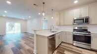 Located at 2 Walter Ave in Highland Park, NJ, this thoughtfully designed single-floor residence offers a clean, modern aesthetic throughout. The open-concept living and kitchen area serves as the heart of the home, where wood-look flooring flows seamlessly underfoot and recessed lighting creates a bright, welcoming atmosphere. The kitchen is equipped with soft-tone shaker cabinetry, white quartz countertops, a peninsula island with an undermount sink, and a full suite of stainless steel appliances including a gas range, microwave, dishwasher, and refrigerator. Elegant pendant lighting with brass accents hangs above the island, adding a refined touch to the space. The living area extends generously from the kitchen, offering ample room for comfortable furnishing arrangements. Bedrooms feature plush wall-to-wall carpeting, ceiling fans, and multiple windows that invite an abundance of natural light and views of the surrounding greenery. The primary bathroom is well-appointed with a double-sink vanity featuring dark countertops, white shaker cabinetry, and a walk-in glass-enclosed shower with a built-in bench. A secondary bathroom provides a single-sink vanity with matching cabinetry and tile flooring. Overall, the space presents a cohesive, contemporary design with high-quality finishes throughout.