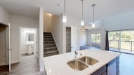 This two-story residence showcases a thoughtfully designed open-concept layout with contemporary finishes throughout. The main level centers around a well-appointed kitchen featuring dark-toned shaker cabinets, a large quartz-topped island with a double basin sink, and stainless steel appliances including a range, microwave, and refrigerator. Pendant lighting illuminates the island, while recessed lighting brightens the surrounding space. The kitchen flows seamlessly into the living area, which is fitted with a ceiling fan and access to an outdoor balcony with views of surrounding greenery. A bathroom and pantry storage are also conveniently located on this level, along with wood-look plank flooring that carries throughout the main living areas.

A staircase leads to the upper level, where carpeted bedrooms and a spacious landing hallway provide comfort and privacy. The upper level includes bedrooms equipped with wall-mounted climate control units and generous closet space, including a walk-in closet with wire shelving. A full bathroom on this level offers a white quartz vanity, large mirror, soaking tub, and wood-look tile flooring. A dedicated laundry area with in-unit washer hookups completes the home's functional and well-organized layout.