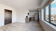Unit 304 is a well-appointed 1-bedroom, 1-bathroom residence with a clean, modern aesthetic carried consistently throughout the space. Light-toned wood-style flooring runs through the open-concept living and kitchen area, contributing to a bright, airy atmosphere enhanced by white walls and natural light from large windows.

The kitchen is efficiently designed and features two-tone cabinetry — white upper cabinets paired with warm wood-grain lower cabinets — and a light stone-look countertop. A full suite of stainless steel appliances includes a range, over-the-range microwave, refrigerator, and dishwasher, making it both functional and visually cohesive.

The living area is open and flexible, with a wall-mounted mini-split system providing climate control. A dark wood-accented entry door adds a refined contrast to the otherwise light interior palette.

The bedroom is carpeted for comfort and features multiple large windows that allow generous natural light and urban views. A wall-mounted mini-split unit provides dedicated climate control in this room as well.

The bathroom offers a clean, contemporary finish with wood-look tile flooring, a white floating vanity, and a glass-enclosed shower with stone-tile surround. In-unit laundry is also included, adding everyday convenience to this thoughtfully finished residence.