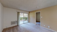 Located at 2372 Lucretia Ave in San Jose, California, this single-floor unit offers a practical and functional layout across several distinct spaces. The living area is carpeted and bathed in natural light, courtesy of a large sliding glass door that opens to an outdoor patio overlooking greenery. A wall-mounted air conditioning unit provides climate control, and a textured ceiling runs throughout the space. An interior doorway connects the living area to additional rooms, creating a cohesive flow.

The kitchen is efficiently arranged in a galley-style configuration, featuring wood cabinetry, a white electric range, an under-cabinet range hood, and a stainless steel sink positioned beneath a window that lets in natural light. A bold red accent wall adds visual contrast against the wood tones. A pass-through or peninsula area connects the kitchen to the adjacent carpeted living space, which is brightened by a pendant light fixture. A refrigerator and ample upper and lower cabinetry complete the kitchen's storage options.

The bedroom is generously sized with plush carpet, neutral walls, and built-in closets offering practical storage. The bathroom features tile flooring, a toilet, and a shower-tub combo enclosed by sliding glass doors, maintaining a clean, utilitarian aesthetic throughout.