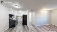 This 2-bedroom, 2-bathroom residence in Greenville, NC offers a practical and modern single-floor layout with clean, neutral finishes throughout. The open-concept kitchen and living area serves as the heart of the home, featuring wood-look luxury vinyl plank flooring, white cabinetry with light countertops, and black appliances including a refrigerator and range. A stacked washer and dryer unit is conveniently located within the kitchen area. The living room is bright and open, with natural light filtering through windows fitted with blinds and a wall-mounted light fixture for additional illumination. A connecting hallway leads to both bedrooms and the bathrooms. The primary bedroom offers a generous footprint with plush carpeting, a ceiling fan with light kit, and a window with outdoor views. The second bedroom also features carpet and a windowed wall, with access to a dedicated closet. Both bathrooms are finished in a crisp, all-white palette — one includes a tub-shower combination, while the other showcases a sleek vanity with an undermount sink, round mirror, and contemporary brushed nickel fixtures. Wood-look flooring carries through the bathrooms, tying the space together cohesively. Textured ceilings and neutral wall tones complete the clean, move-in-ready aesthetic throughout.