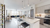 This thoughtfully designed two-bedroom, three-bathroom residence offers a bright, open-concept floor plan with contemporary finishes throughout. The living and dining areas flow seamlessly together, bathed in natural light from large windows dressed with sheer curtains and blinds. Light-toned hardwood-style flooring extends throughout the main living spaces, enhancing the clean, modern aesthetic.

The kitchen is a standout feature, equipped with stainless steel appliances, two-tone cabinetry in warm gray and light wood tones, a tile backsplash, and a generously sized island with quartz countertops and pendant lighting — ideal for casual dining or entertaining. The adjacent dining area accommodates a full dining table beneath a statement chandelier.

The primary bedroom receives abundant natural light and opens to an outdoor balcony with open views. The en-suite bathroom features tile flooring, warm wood cabinetry, and a clean, neutral palette. The second bedroom offers a calm atmosphere with a soft accent wall and ample natural light. A dedicated laundry room houses a full-size side-by-side washer and dryer. The three bathrooms are finished with large-format tile surrounds and modern fixtures, completing this polished, well-appointed residence.