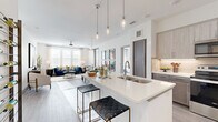 This thoughtfully designed two-bedroom, three-bathroom residence offers a bright, open-concept floor plan with contemporary finishes throughout. The living and dining areas flow seamlessly together, bathed in natural light from large windows dressed with sheer curtains and blinds. Light-toned hardwood-style flooring extends throughout the main living spaces, enhancing the clean, modern aesthetic.

The kitchen is a standout feature, equipped with stainless steel appliances, two-tone cabinetry in warm gray and light wood tones, a tile backsplash, and a generously sized island with quartz countertops and pendant lighting — ideal for casual dining or entertaining. The adjacent dining area accommodates a full dining table beneath a statement chandelier.

The primary bedroom receives abundant natural light and opens to an outdoor balcony with open views. The en-suite bathroom features tile flooring, warm wood cabinetry, and a clean, neutral palette. The second bedroom offers a calm atmosphere with a soft accent wall and ample natural light. A dedicated laundry room houses a full-size side-by-side washer and dryer. The three bathrooms are finished with large-format tile surrounds and modern fixtures, completing this polished, well-appointed residence.