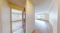 Located at 101 W Olympic Place in Seattle's Queen Anne neighborhood, this one-bedroom, one-bathroom unit offers a practical and well-organized layout across a single floor. The open living area is a standout feature, characterized by light hardwood flooring that runs throughout and large windows that allow natural light to fill the space while providing views of the surrounding neighborhood. A baseboard heating system lines the perimeter of the living area, ensuring year-round comfort.

The kitchen is positioned adjacent to the living space and features dark espresso-toned cabinetry — both upper and lower — paired with light countertops and a stainless steel sink. A window in the kitchen brings in additional natural light. Appliances including a refrigerator and range are included.

The bedroom is a comfortable, well-proportioned room with soft carpeting, a sliding closet, and a window for natural light. Its warm-toned wood door adds a classic touch to the space.

The bathroom features a full tub and shower combination surrounded by distinctive pink ceramic tile, lending a retro character to the space. Overall, the unit maintains a clean, neutral palette throughout, creating a bright and functional living environment.