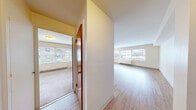 Located at 101 W Olympic Place in Seattle's Queen Anne neighborhood, this one-bedroom, one-bathroom unit offers a practical and well-organized layout across a single floor. The open living area is a standout feature, characterized by light hardwood flooring that runs throughout and large windows that allow natural light to fill the space while providing views of the surrounding neighborhood. A baseboard heating system lines the perimeter of the living area, ensuring year-round comfort.

The kitchen is positioned adjacent to the living space and features dark espresso-toned cabinetry — both upper and lower — paired with light countertops and a stainless steel sink. A window in the kitchen brings in additional natural light. Appliances including a refrigerator and range are included.

The bedroom is a comfortable, well-proportioned room with soft carpeting, a sliding closet, and a window for natural light. Its warm-toned wood door adds a classic touch to the space.

The bathroom features a full tub and shower combination surrounded by distinctive pink ceramic tile, lending a retro character to the space. Overall, the unit maintains a clean, neutral palette throughout, creating a bright and functional living environment.