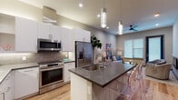 Located at 1825 Park Avenue in Dallas, TX, this single-floor residence showcases a contemporary design with an open-concept layout that seamlessly connects the kitchen, dining, and living areas. Light-toned hardwood flooring runs throughout, lending warmth and continuity to the space.

The kitchen is a standout feature, equipped with stainless steel appliances, white flat-panel cabinetry, and a grey tile backsplash. A large central island with dark quartz countertops provides generous prep and seating space, complemented by striking cylindrical pendant lights overhead. The open sightlines from the kitchen into the living area enhance the sense of spaciousness.

The living area is bright and inviting, benefiting from large windows with slatted blinds that allow natural light to filter in. A wall-mounted electric fireplace adds a modern focal point, while a direct-access door connects the space to the exterior.

The bathroom is finished in marble-look tile and features a glass-enclosed walk-in shower, a vanity with undermount sink, and clean, neutral tones that contribute to a spa-like atmosphere. Overall, the space delivers a cohesive, modern aesthetic with high-quality finishes throughout.