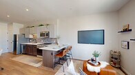 Located at 615 E Corcoran Ave in Milwaukee, WI, this thoughtfully designed one-bedroom, one-bathroom unit maximizes every inch of its compact footprint. The open-concept layout seamlessly connects the kitchen, dining, and living areas, creating a functional and cohesive living space throughout. The kitchen is a standout feature, showcasing two-tone cabinetry — white upper cabinets paired with rich dark lower cabinets — complemented by a subtle tile backsplash, quartz countertops, stainless steel appliances, and an undermount sink with a matte black faucet. A peninsula with bar seating provides a natural transition into the living area, which is anchored by a wall-mounted TV and a ceiling fan. Large windows flood the space with natural light while offering impressive Milwaukee skyline views. Light-toned hardwood flooring runs throughout, enhancing the bright, airy ambiance. The bedroom is generously proportioned, featuring large windows that continue the skyline views and a ceiling fan overhead. The bathroom includes a dark-cabinetry vanity with quartz countertop and a stacked washer and dryer unit for added convenience. A dedicated closet with built-in wire shelving provides organized storage, and the unit's stylish blue entry door adds a distinctive finishing touch.