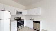 This well-appointed single-floor unit offers a clean, modern aesthetic throughout, with a neutral color palette and thoughtful finishes that create a bright and welcoming atmosphere. The kitchen is a standout feature, outfitted with a full suite of stainless steel appliances including a refrigerator, electric range, over-the-range microwave, and dishwasher. Crisp white cabinetry extends to the upper and lower walls, providing generous storage, while light-toned countertops and a stainless steel sink complete the functional workspace. Light wood-style flooring flows through the kitchen and living areas, contributing to the space's airy, contemporary feel. The open living area benefits from a large window that invites ample natural light and provides views of the surrounding outdoors. The bedroom features soft carpeting and a sliding closet door, offering a comfortable and quiet retreat. The bathroom is efficiently designed, housing a full tub-and-shower combo, toilet, and a vanity with a white countertop and storage cabinetry. A stacked washer and dryer unit is conveniently integrated within the bathroom, adding practical in-unit laundry access. Overall, the space combines functional design with modern finishes to deliver a clean and comfortable living environment.