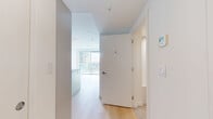 Located at 5670 Cambie St in Vancouver, BC, this well-appointed one-bedroom, one-bathroom unit offers a thoughtfully designed layout across a single floor. The interior is finished in a clean, modern palette of whites and warm neutrals, with light hardwood flooring flowing throughout the main living areas and bedroom.

The kitchen is a standout feature, showcasing flat-panel cabinetry in white and soft grey tones, a light stone composite countertop with a peninsula for additional workspace, a pale blue glass backsplash, and stainless steel appliances including a refrigerator, range, and dishwasher. Recessed lighting and open shelving complete the contemporary aesthetic.

The living area benefits from large floor-to-ceiling sliding glass doors that open to a balcony, inviting an abundance of natural light and offering views of the surrounding Vancouver cityscape. The bedroom is a quiet, bright space featuring sliding closet doors and the same warm hardwood flooring, providing practical storage within a compact footprint.

The bathroom is finished with neutral stone-toned tile flooring, a modern floating vanity with a vessel sink, stone-finish countertop, and a mirrored medicine cabinet, reflecting a consistent attention to clean, functional design. A welcoming hallway connects all rooms efficiently. The overall ambiance is bright, minimalist, and modern.