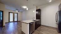 This single-story residence showcases a contemporary design with a thoughtful layout and quality finishes throughout. The open-concept kitchen serves as a central highlight, featuring dark espresso cabinetry that extends to the ceiling for ample storage, granite-look countertops, a peninsula with an undermount sink, stainless steel appliances, and a herringbone tile backsplash. Pendant lighting and track lighting illuminate the workspace, which flows seamlessly into the living area. The living space is equipped with a ceiling fan and provides access to an outdoor area through glass French doors fitted with blinds, allowing natural light to filter in.

A dedicated mudroom area near the entry offers a built-in bench with storage cubbies and wall-mounted hooks, providing a practical transition space. The bedroom is carpeted and includes a window with blinds for natural light. The primary bathroom is well-appointed with a double-sink vanity topped with granite-look counters, dark cabinetry, a large framed mirror, a glass-enclosed shower, and tile flooring. A walk-in closet with built-in shelving and hanging rods is accessible directly from the bathroom. Wood-style plank flooring runs throughout the main living areas, tying the space together with a warm, cohesive aesthetic.