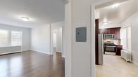 Located at 510 Millburn Ave in Short Hills, NJ, this one-bedroom, one-bathroom unit on the third floor offers a thoughtfully arranged layout across a single level. Rich hardwood flooring flows throughout the main living areas, creating a warm and cohesive aesthetic.

The living room is a generously sized, open area with neutral white walls and clean baseboard trim, providing a versatile canvas for furnishing. It connects seamlessly to the rest of the unit via a central hallway. The hallway is lined with textured walls and hardwood flooring underfoot, lending a defined sense of arrival and transition between spaces.

The kitchen is well-appointed with dark espresso cabinetry, granite-style countertops, a tile backsplash with decorative accent border, and stainless steel appliances including a gas range, over-the-range microwave, and refrigerator. Light tile flooring completes the kitchen's polished look.

The bedroom is a comfortable, well-proportioned room with hardwood floors, soft neutral walls, and two white panel doors providing access to a closet and the hallway.

The bathroom features floor-to-ceiling tile surrounding a soaking tub and shower combination, with a decorative mosaic accent border, built-in corner shelving, and a window for natural light — offering a clean, spa-like feel.