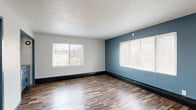 Located at 262 Birmingham St in Saint Paul, MN, this one-bedroom, one-bathroom unit offers a practical and efficiently designed single-floor layout. The main living area is the largest space in the unit, featuring rich wood-look laminate flooring, dark baseboard trim, and a textured ceiling. A striking teal-blue accent wall anchors the room, complemented by multiple large windows fitted with horizontal blinds that allow natural light to filter throughout the space. The entry door, painted in a matching blue-gray tone, adds a cohesive design touch. The kitchen area is compactly arranged with a white gas range, a stainless steel sink, blue lower cabinetry, and white upper cabinets — all framed by blue-trimmed doorways that connect the spaces. A hallway leads to the bedroom, which is generously proportioned relative to the overall footprint and continues the same wood-look flooring and windowed blue accent wall found in the main area. The bathroom is clean and functional, featuring full white square tile surrounding a soaking tub with shower, a pedestal-style vanity with a matte black faucet, and a window that brings in natural light. Tile flooring in a neutral diamond pattern completes the bathroom's practical design.