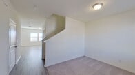 This two-story home features a clean, contemporary design with neutral finishes carried consistently throughout both levels. The main floor showcases a well-appointed kitchen as its standout space, equipped with crisp white shaker-style cabinetry, granite countertops with subtle veining, and a full suite of stainless steel appliances including a range, over-the-range microwave, and refrigerator. A central island with an undermount sink adds functional workspace and casual dining potential. Wood-look hard flooring runs through the kitchen and main living areas, providing durability and visual continuity.

A staircase connects the two floors, transitioning into carpeted upper-level spaces. The primary bedroom is generously proportioned, featuring dual windows that admit natural light and views of the surrounding area. The accompanying primary bathroom offers an extended vanity with ample cabinetry, a large mirror with overhead lighting, a walk-in shower, and direct access to a spacious walk-in closet outfitted with wire shelving and hanging rods. A secondary bathroom on the upper level includes a tub-shower combination and a white vanity. Additional carpeted rooms provide flexible space suitable for bedrooms or other uses. Throughout, the home maintains a bright, move-in-ready aesthetic with white walls and consistent trim detailing.