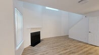 This two-story, 1-bedroom, 1-bathroom home is thoughtfully designed across two well-proportioned floors. The main level combines the living room and kitchen, while the upper level is dedicated entirely to the primary bedroom suite.

The living room is an immediate standout, featuring soaring vaulted ceilings that amplify the sense of space, a striking black fireplace with a clean white mantle, and a high clerestory skylight window that floods the room with natural light. Light wood-look flooring runs throughout the main level, complementing the bright white walls. Multiple windows fitted with blinds further enhance the airy atmosphere, and a staircase leads to the upper floor.

The galley-style kitchen is well-appointed with crisp white shaker cabinetry, speckled granite countertops, stainless steel appliances including a range, microwave, and refrigerator, and a double-basin sink. A peninsula counter offers additional workspace and visual separation from the living area.

The generously sized primary bedroom on the upper level is carpeted for comfort and includes a ceiling fan, a large sliding door with vertical blinds, and additional windows that bring in natural light. A built-in niche adds architectural character. The en-suite bathroom features white cabinetry topped with granite countertops and a brushed nickel faucet and fixtures, maintaining the home's clean, modern aesthetic throughout.