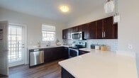 Located at 6400 Preserve Crossing Blvd N in Gahanna, Ohio, this multi-level home spans three floors and offers a well-designed layout with consistent, modern finishes throughout. The main living level features durable hardwood-style flooring that flows seamlessly from the open living area through to the kitchen. A staircase with a painted wood railing connects the levels, reinforcing the home's clean, contemporary aesthetic.

The kitchen is a standout space, outfitted with rich dark espresso cabinetry, crisp white quartz countertops, and a classic subway tile backsplash. A large kitchen island provides additional prep and gathering space. Stainless steel appliances, including a range, over-the-range microwave, and dishwasher, complete the functional and stylish setup. A window above the sink invites natural light into the space.

The main level also includes a convenient half bathroom featuring a pedestal sink, oval mirror, and neutral gray walls. Upper-level bedrooms are finished with plush carpeting, soft gray walls, and windows that allow in natural light. A full bathroom on the upper level includes a tub-shower combination with a white vanity. The lower level adds additional flexible living space, also with hardwood-style flooring, suitable for a variety of uses.