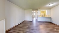 This one-bedroom, one-bathroom unit in Tacoma, Washington offers a practical and comfortable single-floor layout. The living room features wood-look laminate flooring, a textured ceiling, and a sliding glass door that fills the space with natural light while providing a view of the surrounding greenery. A baseboard heating system runs along the walls, ensuring warmth throughout. The open layout connects the living area to a hallway that leads to the kitchen, which features a pass-through counter, white cabinetry, and standard appliances. The bedroom is finished with plush carpeting, a large window with blinds that frames outdoor views, and its own baseboard heater. A dedicated closet with utility access is conveniently located off the bedroom. The bathroom is clean and efficiently designed, featuring wood-look vinyl flooring, a full tub and shower combination with a curved curtain rod, a toilet, and a vanity with countertop. A hallway connects all rooms, providing a logical and functional flow throughout the unit. Textured ceilings are consistent throughout the space, adding a classic residential character to this well-organized Tacoma home.