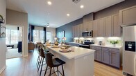 This well-appointed single-floor residence offers a thoughtfully designed open-concept layout that seamlessly connects the kitchen, dining, and living areas. The kitchen is a standout feature, showcasing floor-to-ceiling gray shaker-style cabinetry, a classic white subway tile backsplash, and a full suite of stainless steel appliances including a French door refrigerator, electric range with over-the-range microwave, and dishwasher. A generously sized center island with a white quartz countertop and built-in sink provides ample prep space and casual bar seating. Light wood-tone flooring runs throughout the main living areas, lending warmth and continuity to the space. The living room benefits from natural light streaming through large windows and a glass door that opens to an outdoor view, complemented by a ceiling fan and neutral wall tones accented by a rich blue feature wall. The bedroom is carpeted for comfort, offering a quiet retreat with a window and space for ample furnishings. The full bathroom features a soaking tub with tiled surround, a gray vanity with white countertop, and direct access to a dedicated in-unit laundry area with stacked washer and dryer. The overall design palette is modern and cohesive, combining function with contemporary style.