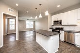 This single-floor unit offers a practical and modern layout across three bedrooms, one bathroom, a kitchen, living room, and dedicated laundry room. The open-concept kitchen serves as a centerpiece, featuring white shaker cabinetry, a classic subway tile backsplash, dark granite countertops, a sizeable island with pendant lighting, and a full suite of stainless steel appliances including a refrigerator, range, microwave, and dishwasher. The kitchen flows naturally into the living area, which is finished with wood-style flooring and neutral-toned walls, creating a cohesive and airy feel. Natural light enters through multiple windows, offering views of the surrounding neighborhood. The bedrooms are finished with either soft carpeting or wood-style flooring, and each features windows that bring in additional light. The bathroom includes a white vanity with granite countertops, a mirror, and wood-style flooring consistent with the rest of the unit. The laundry room provides in-unit washer and dryer hookups alongside wire shelving for added storage. Throughout the unit, clean lines, recessed lighting, and a neutral color palette contribute to a contemporary, move-in-ready aesthetic.