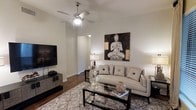 This single-floor residence offers a thoughtfully designed layout that balances comfort and functionality. Rich hardwood flooring flows through the main living areas, creating a warm and cohesive foundation throughout the space. The living room serves as a central gathering area, featuring high ceilings accented by a ceiling fan, neutral-toned walls, and ample room for relaxed seating arrangements. A glass-top coffee table and patterned area rug add texture and depth to the space. The open floor plan connects the living area to a dedicated dining space, ideal for everyday meals and entertaining. The kitchen is positioned conveniently nearby, offering practical access to the living and dining zones. Multiple bedrooms are spread across the layout, each providing generous space and easy access to well-appointed bathrooms. The bathrooms are finished with clean, modern fixtures, including soaking tubs in select rooms. Throughout the residence, the design maintains a calm, neutral palette that lends itself to a serene and welcoming ambiance. The overall layout is efficient and spacious, with clearly defined zones for living, dining, sleeping, and bathing, making this a versatile and comfortable home.