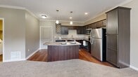 Located in the Yosemite community of Lincoln, Nebraska, this single-floor, one-bedroom, one-bathroom unit delivers a thoughtfully designed layout with modern finishes throughout. The kitchen is a standout feature, showcasing rich dark cabinetry, granite-style countertops, stainless steel appliances including a range, microwave, and refrigerator, and a central island with pendant lighting and crown molding accents. Hardwood-style flooring and an open flow into the living area create a warm, cohesive atmosphere. The living area is carpeted and generously sized, featuring a ceiling fan, crown molding, and a door with adjacent window that invites natural light and outdoor views. The bedroom is comfortably proportioned with plush carpet, a ceiling fan, and a window with blinds providing natural light. It connects to a well-organized walk-in closet outfitted with built-in shelving and hanging rods on multiple sides. The bathroom includes a full tub-shower combo, dark cabinetry vanity with a granite-style countertop, and wood-style flooring. A dedicated laundry area with side-by-side washer and dryer and an overhead storage shelf adds everyday convenience to this well-appointed home.