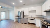 This 1-bedroom, 1-bathroom residence is thoughtfully designed to maximize every square foot of its single-floor layout. The kitchen is a standout feature, showcasing white shaker-style cabinetry extending to the ceiling for ample storage, granite-look countertops, and a full suite of stainless steel appliances including a French door refrigerator with ice and water dispenser, a dishwasher, and a freestanding range. A double basin sink and built-in desk nook add functional versatility to the space. The herringbone-patterned light wood flooring flows seamlessly throughout the unit, lending a clean and contemporary aesthetic. The bedroom is bright and airy, featuring a large window that invites natural light and outdoor views, complemented by a ceiling fan with light fixture and a tray ceiling detail. The bathroom is designed with accessibility in mind, offering a floating dual-sink vanity with granite-look countertops, a wide framed mirror with lighted sconces, grab bars, and an open roll-under vanity space. The overall design is modern and minimalist, with crisp white walls, recessed lighting, and a neutral palette that creates a welcoming and functional living environment.