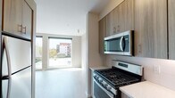 Located on NE Martin Luther King Jr Boulevard in Portland's vibrant Northeast neighborhood, this single-floor unit features a contemporary design with a clean, neutral palette throughout. Light wood-tone flooring runs consistently across the living areas, enhancing the sense of openness and cohesion.

The kitchen is well-appointed with flat-front cabinetry in a warm wood-grain finish, light quartz countertops, a white tile backsplash, and a full suite of stainless steel appliances including a gas range, over-the-range microwave, and dishwasher. The layout flows naturally toward the living area, which is anchored by a pair of large floor-to-ceiling windows that flood the space with natural light and offer views of the surrounding Portland streetscape and neighboring buildings.

A dedicated area within the unit accommodates a stacked washer and dryer, providing convenient in-unit laundry. The bathroom features a full tub-shower combination with chrome fixtures and wood-look flooring, maintaining the unit's consistent modern aesthetic.

Throughout the space, neutral warm-gray walls, clean white trim, and abundant natural light contribute to a bright, contemporary atmosphere well-suited to urban living in Northeast Portland.